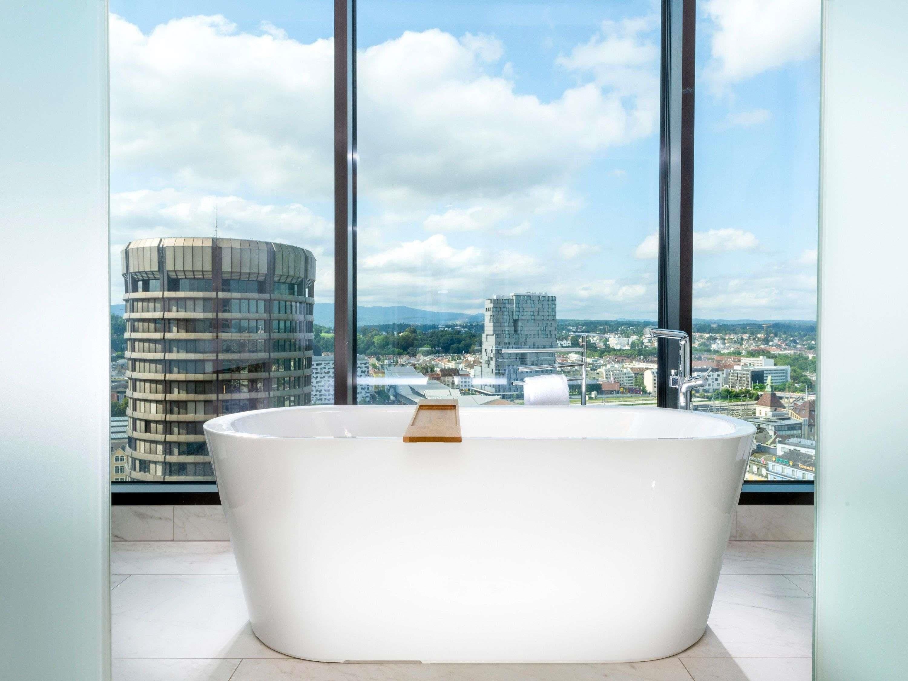 A modern bathroom with a freestanding bathtub and a city view through large windows.