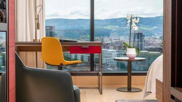 A modern room with a city view, featuring a desk, two chairs, a small table, and a potted orchid.