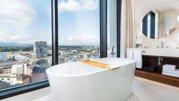 A modern bathroom with a freestanding bathtub, a large mirror, and a city view.