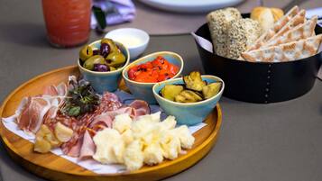 Uma tábua de madeira com diversos queijos, charcutaria, azeitonas e vegetais.
