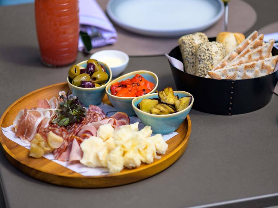 Uma tábua de madeira com diversos queijos, charcutaria, azeitonas e vegetais.