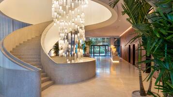 Un hall d’hôtel moderne avec un escalier en colimaçon, un lustre central et un comptoir d’accueil.