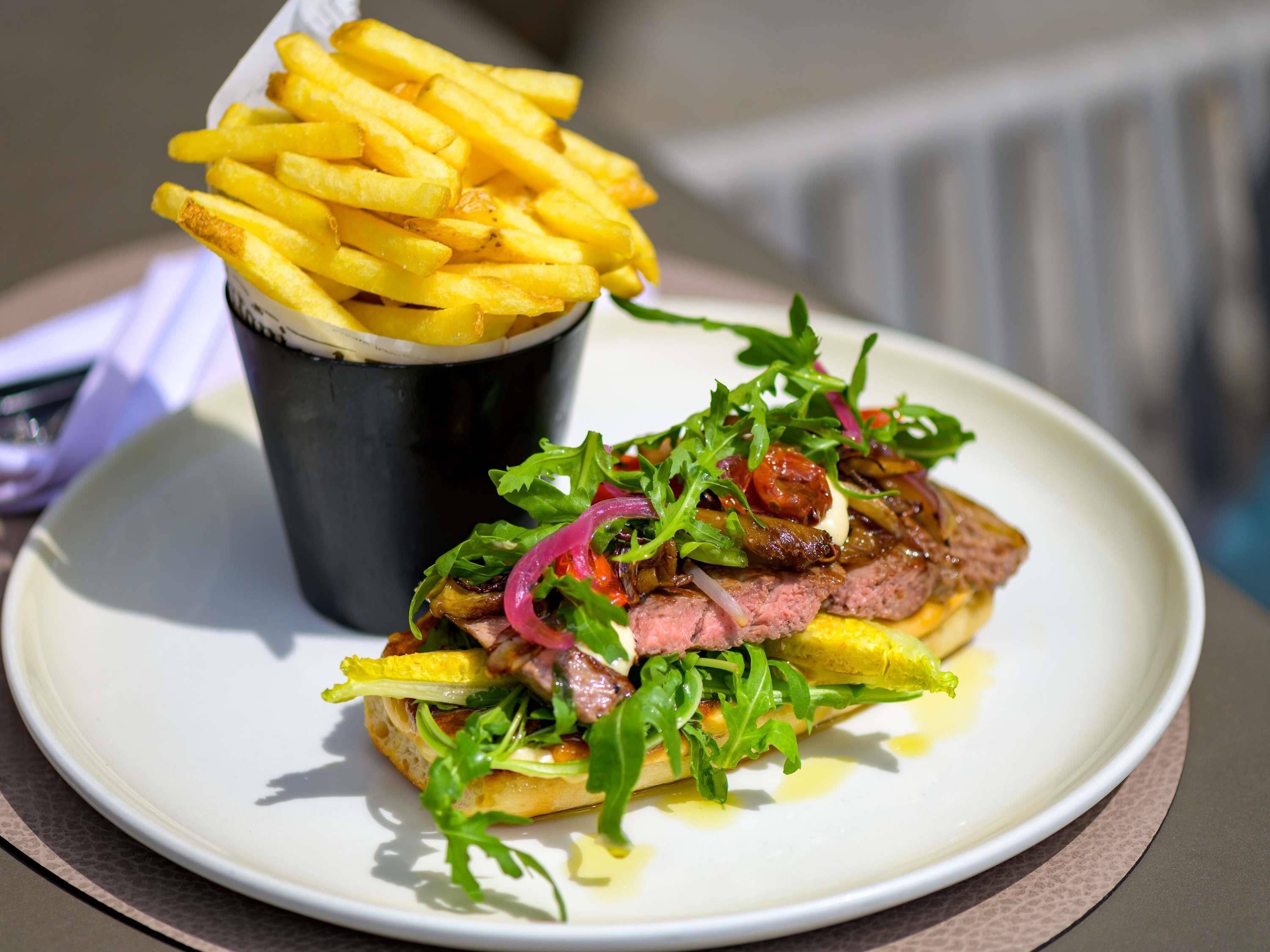 A sandwich with greens and red onions, a side of fries, and a drink in a cup.