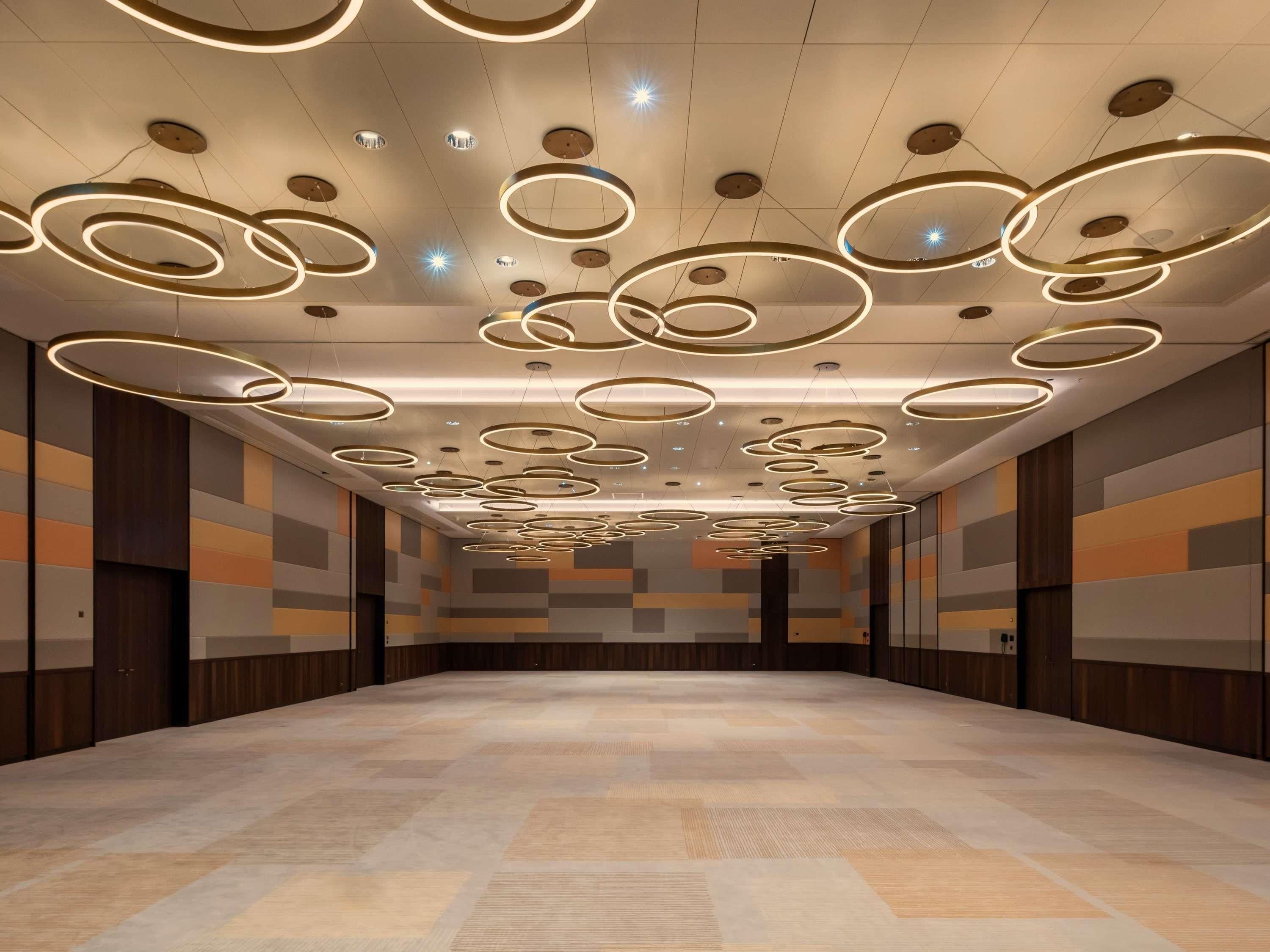 Un pasillo de hotel con un diseño moderno de techo que incluye lámparas circulares y un suelo con diseño.