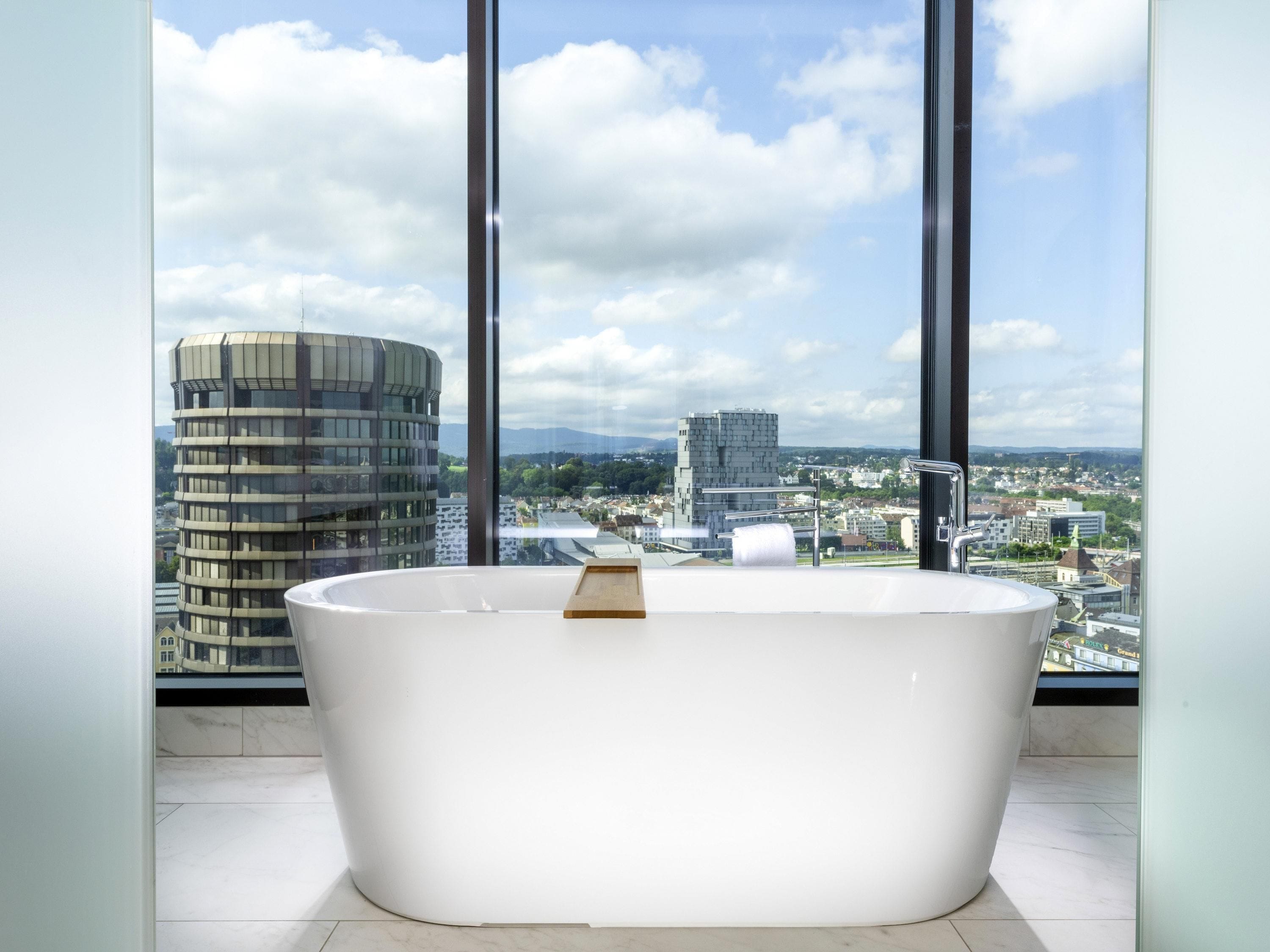 A modern bathroom with a freestanding bathtub, large windows, and a cityscape view.