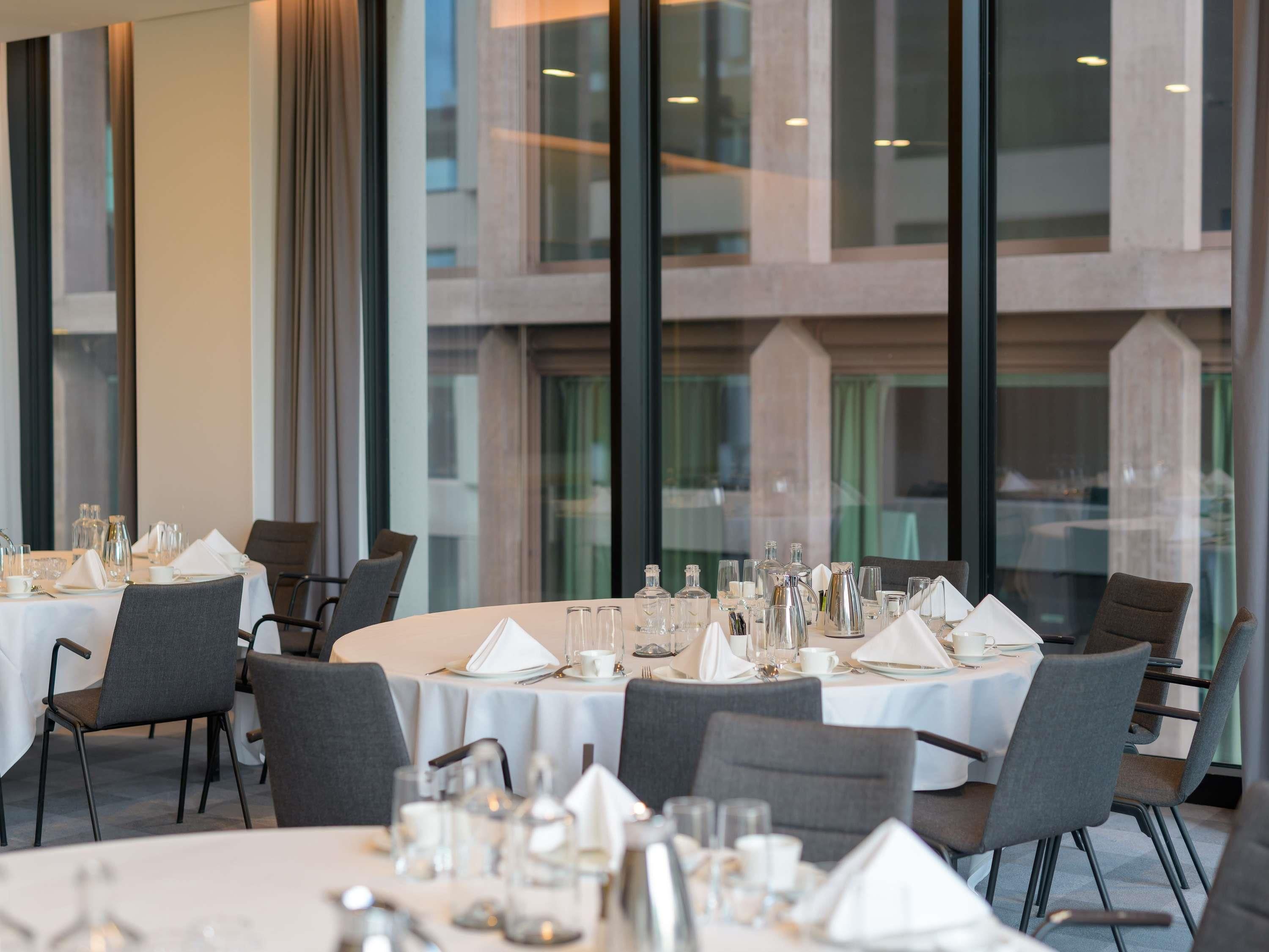 Ein Restaurant mit runden Tischen, großen Fenstern und modernem Interieur.