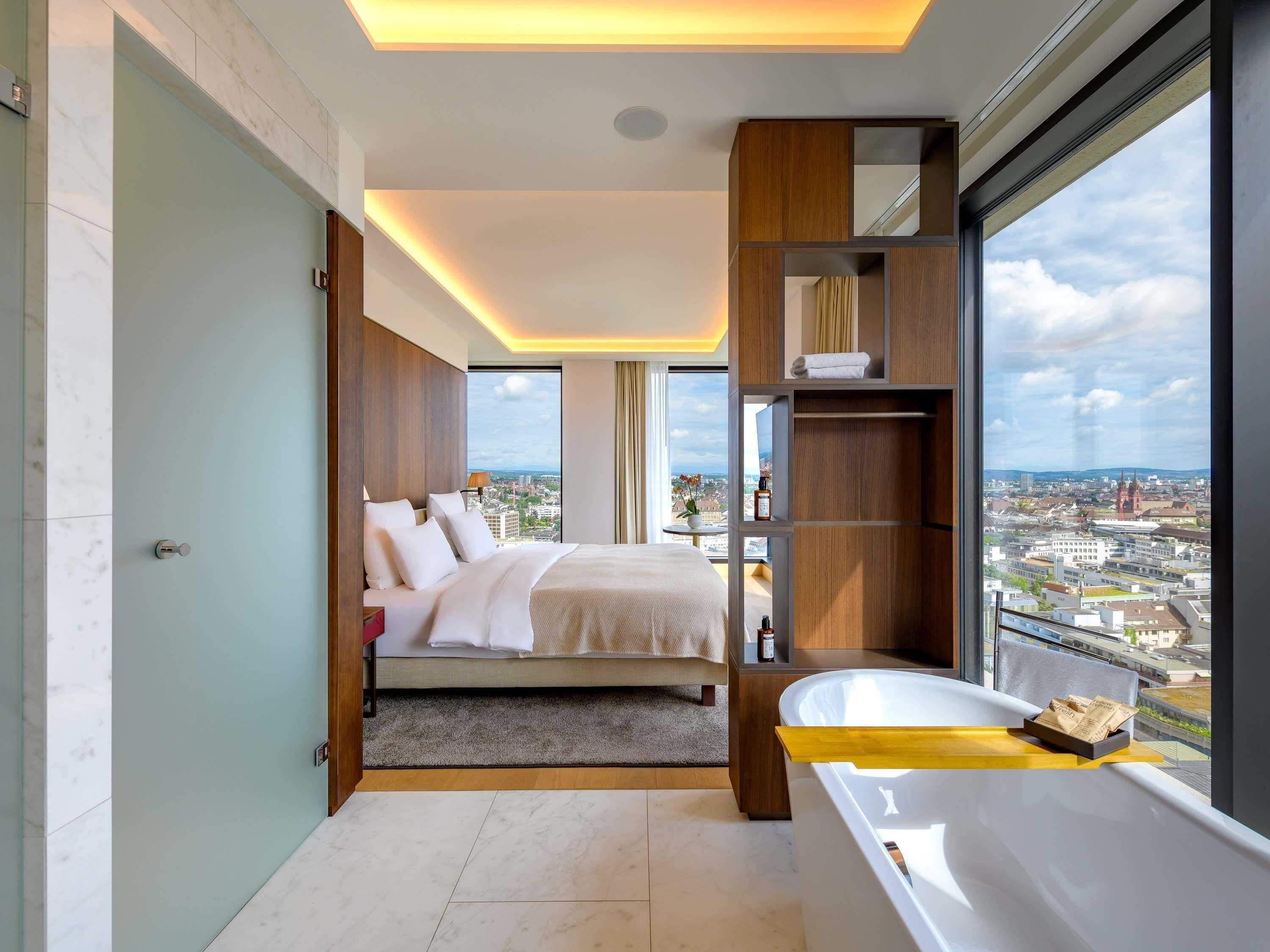 A modern hotel room with a large bed, a bathtub, and a city view.