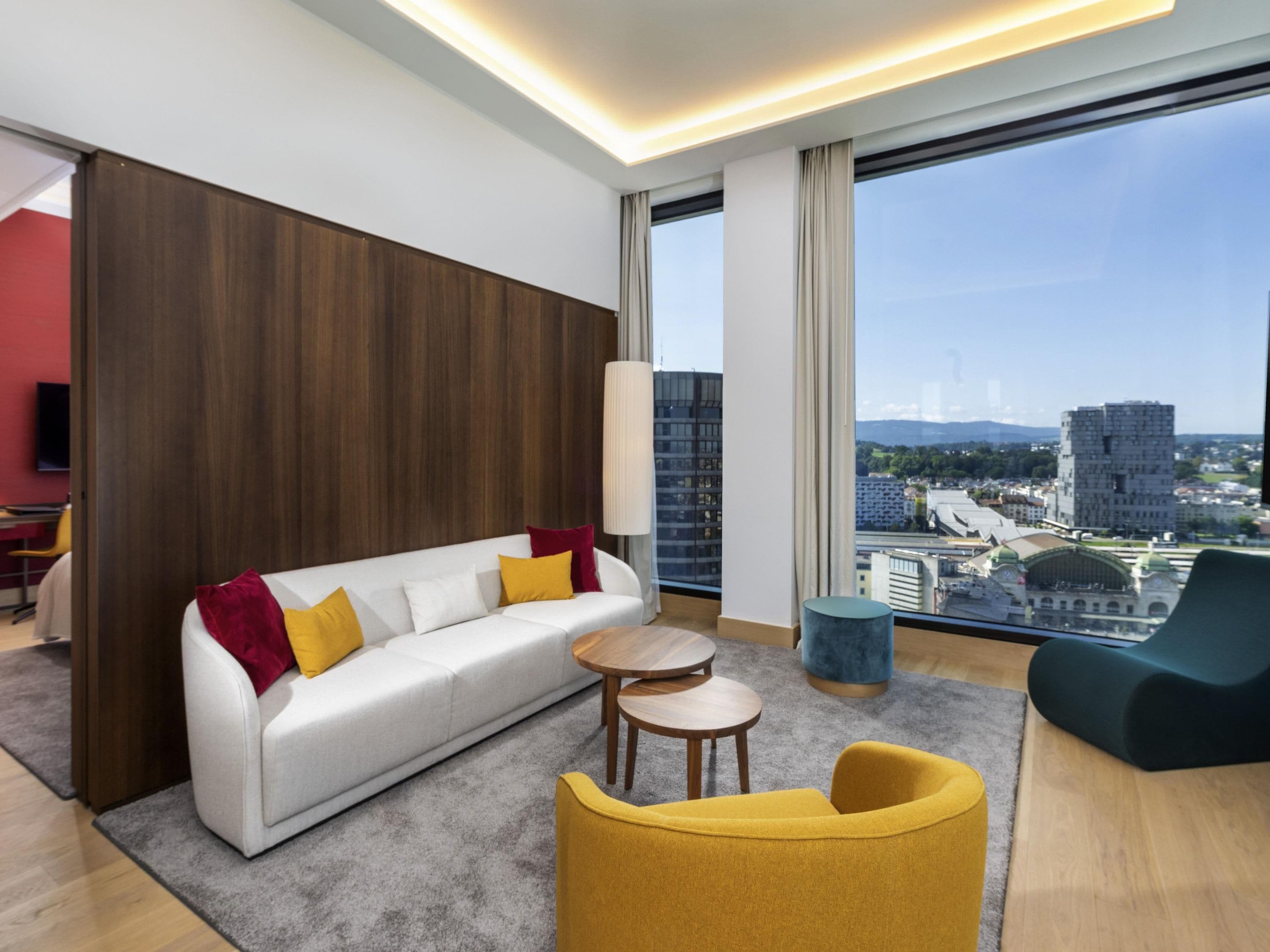 Una sala moderna con un sofá, una mesa redonda de centro y vistas de un paisaje urbano a través de amplios ventanales.