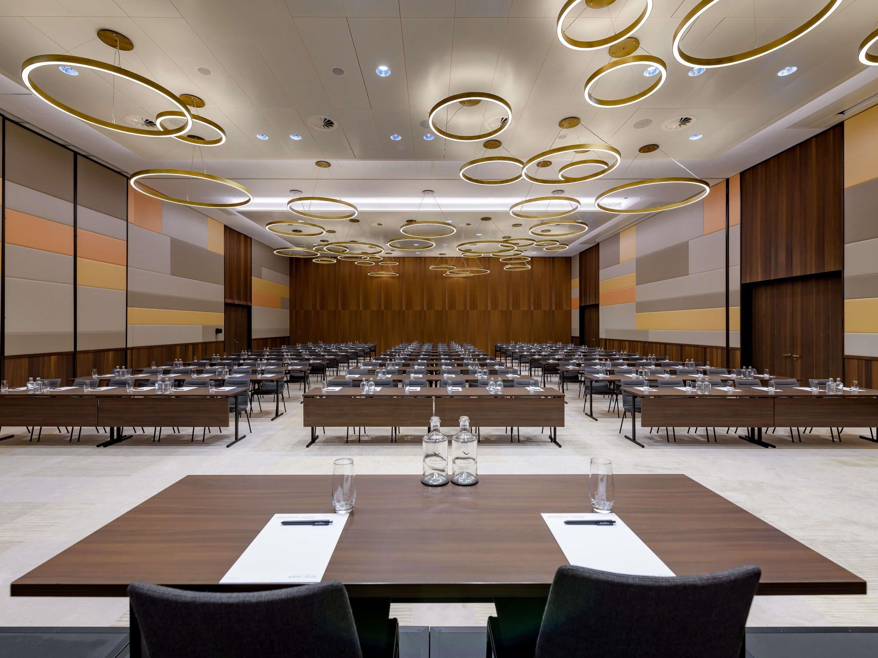 Un salón de conferencias con varias mesas, un diseño moderno del techo y una paleta de colores neutros.