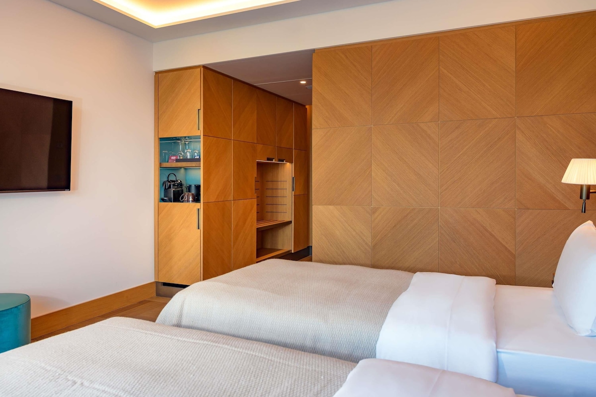 A hotel room with two beds, a wardrobe, a TV, and a lamp.