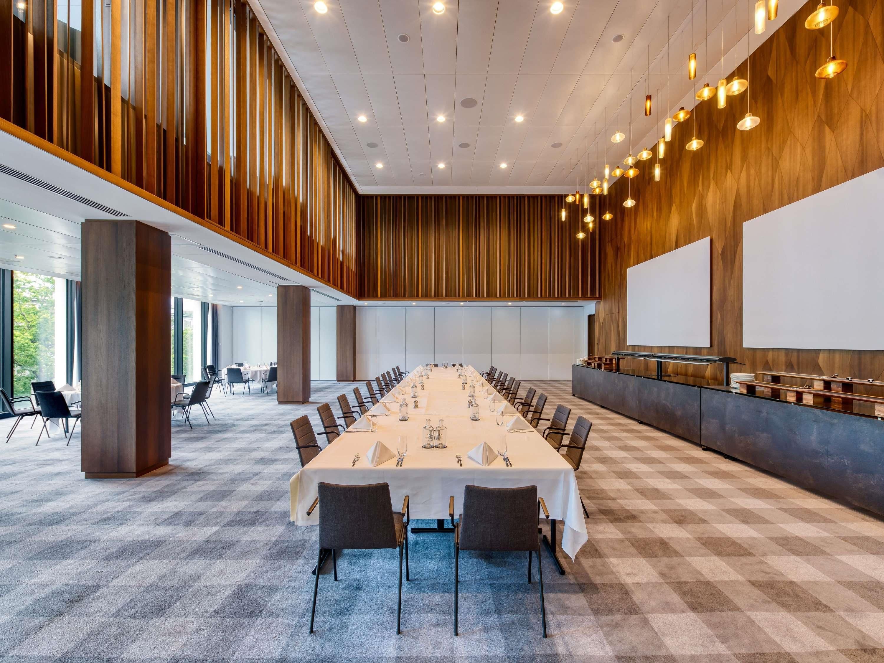 Ett konferensrum med ett långt bord, stolar, en projektorduk och ett stort fönster.