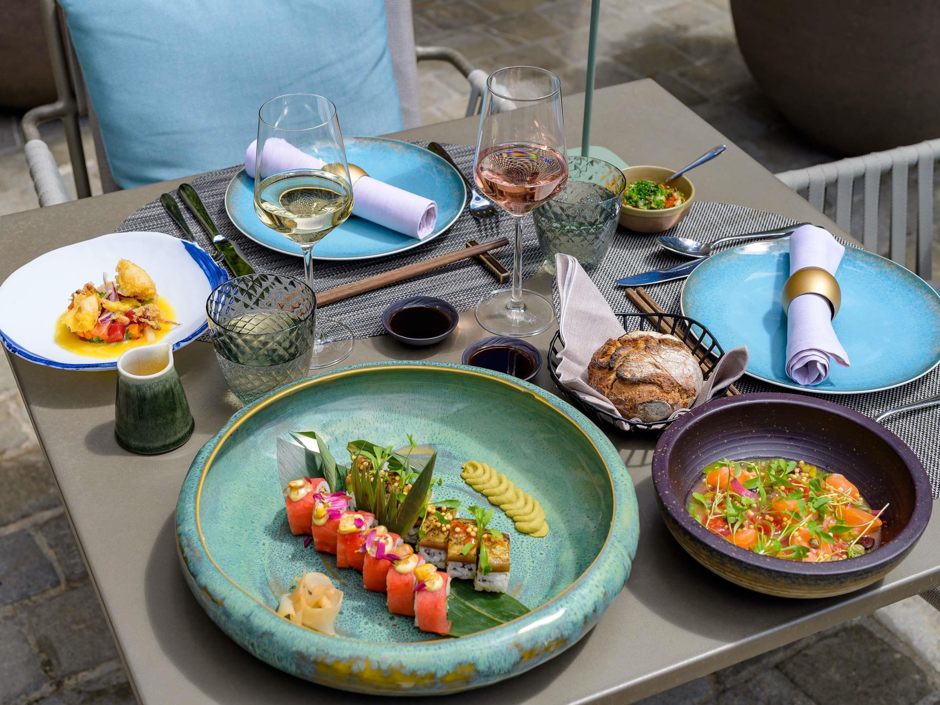 Una mesa lista para una comida, con varios platos, copas de vino y una cesta de pan.