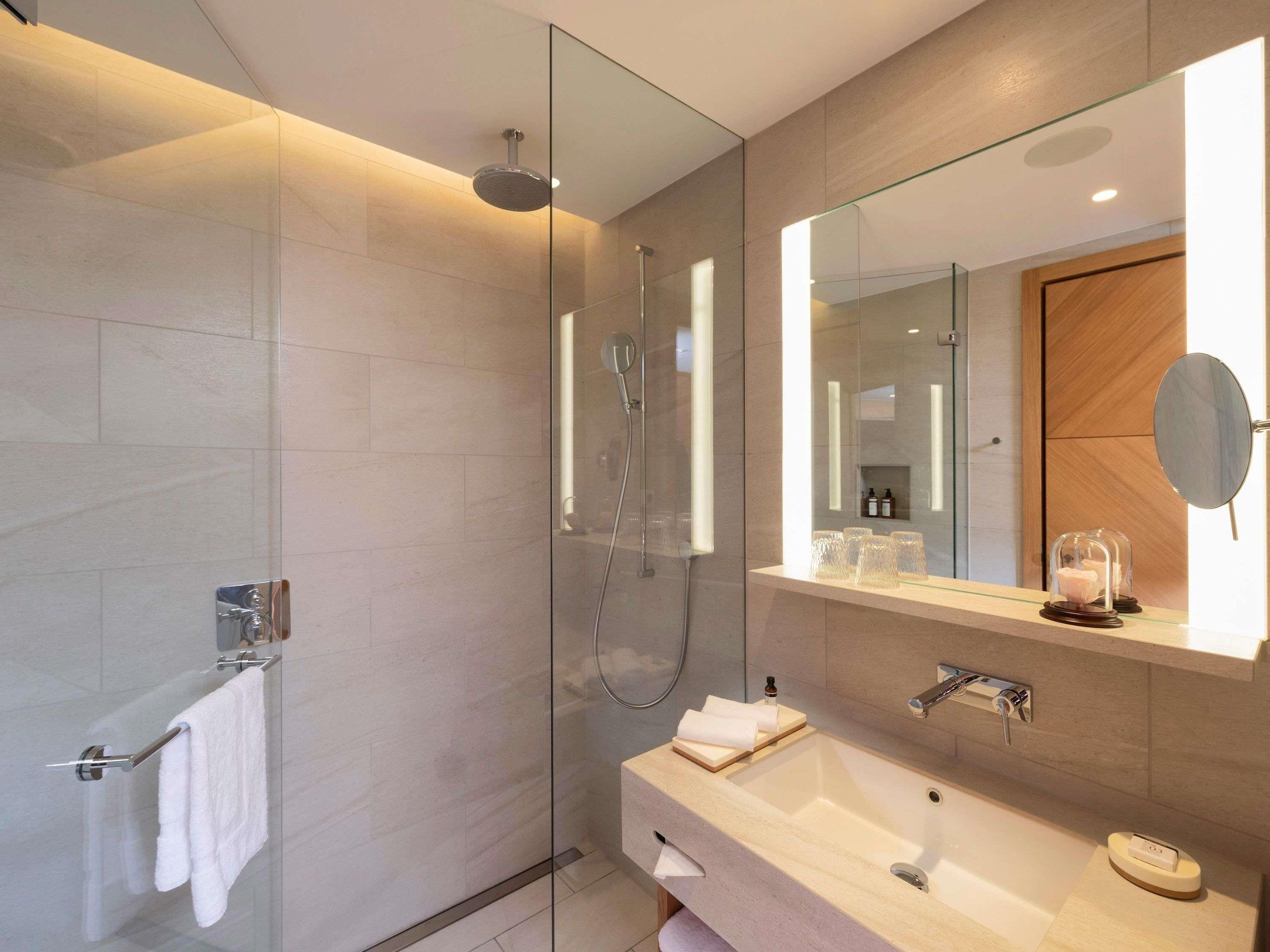 A modern bathroom with a glass-enclosed shower, a large mirror, and a vanity with a sink and towel rack.