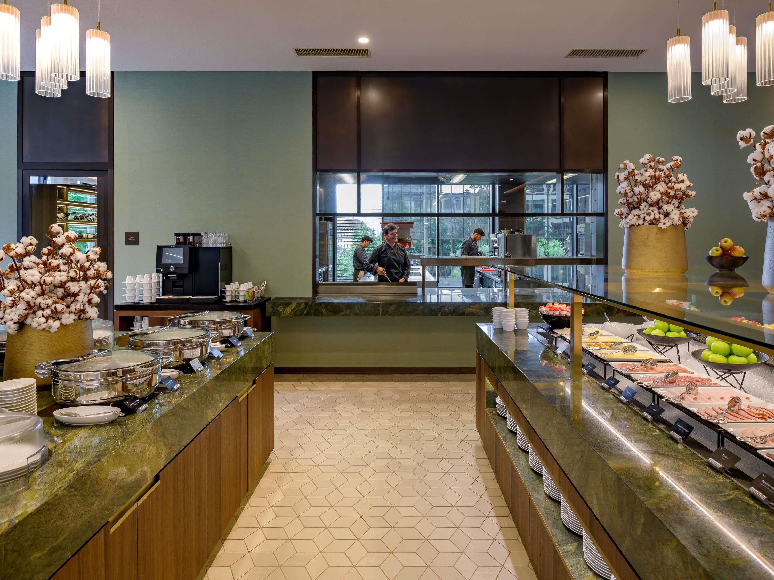 Zona de bufé con diversas opciones de comida, estación de café y área de descanso con vistas al exterior.