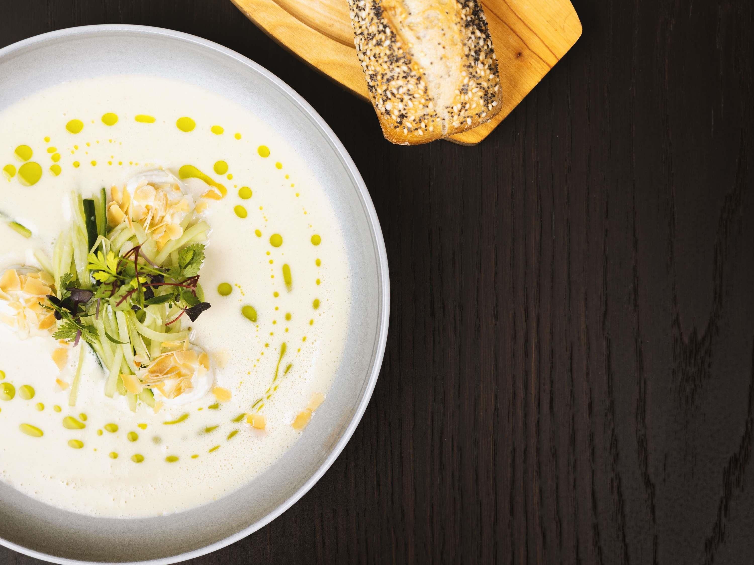 A bowl of soup with a slice of bread on a wooden board.