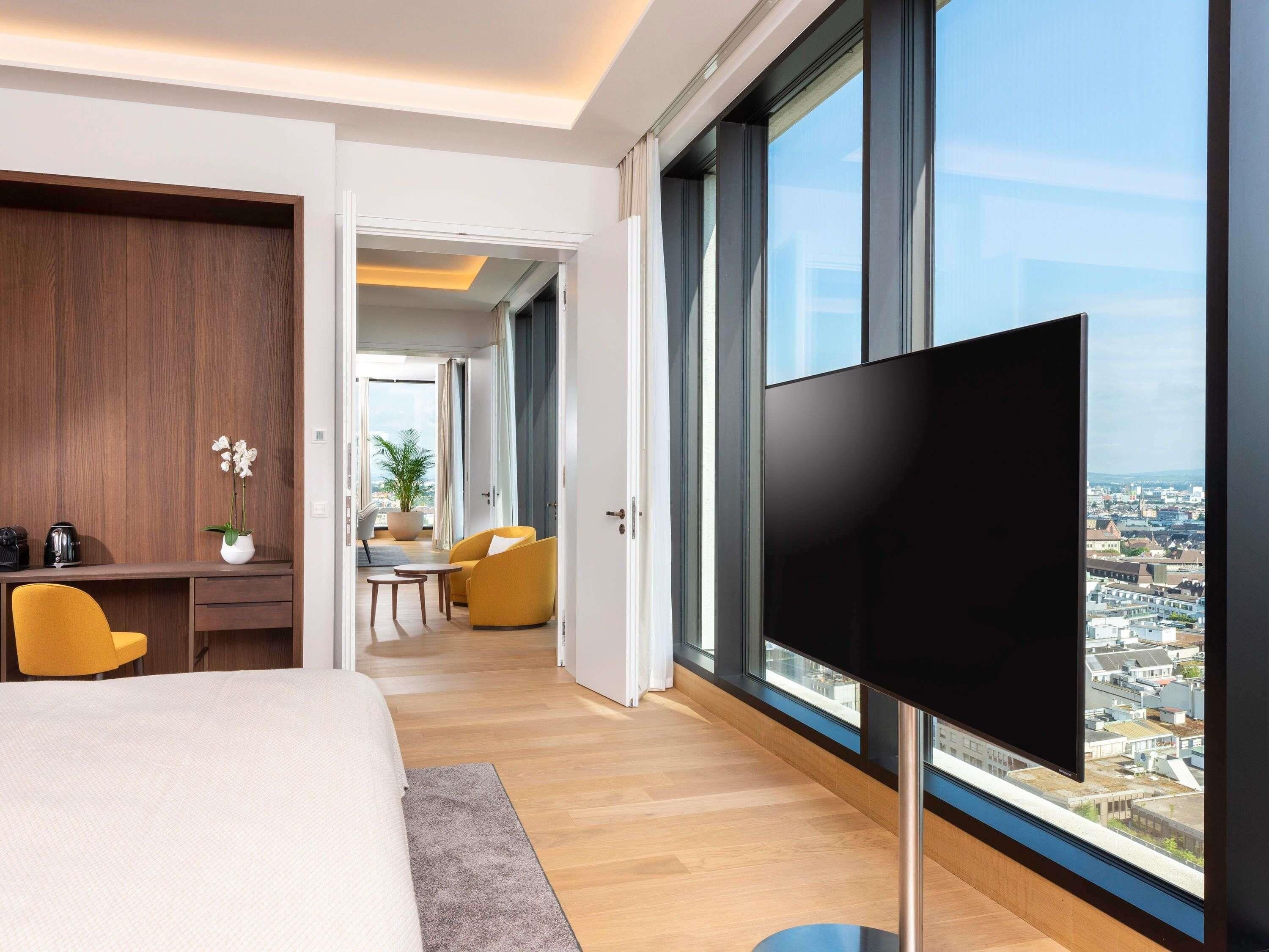 Une chambre d’hôtel moderne équipée d’une grande télévision, d’un lit, d’un bureau et offrant une vue sur la ville.