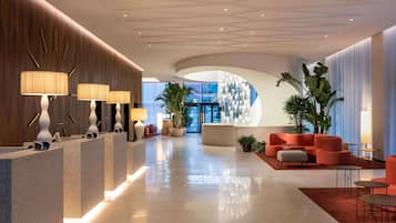 Un hall d’hôtel moderne avec un comptoir d’accueil, un espace salon et une grande plante.