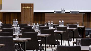 Un salón de conferencias con mesas y sillas, un atril con el nombre del hotel, y botellas de agua sobre las mesas.