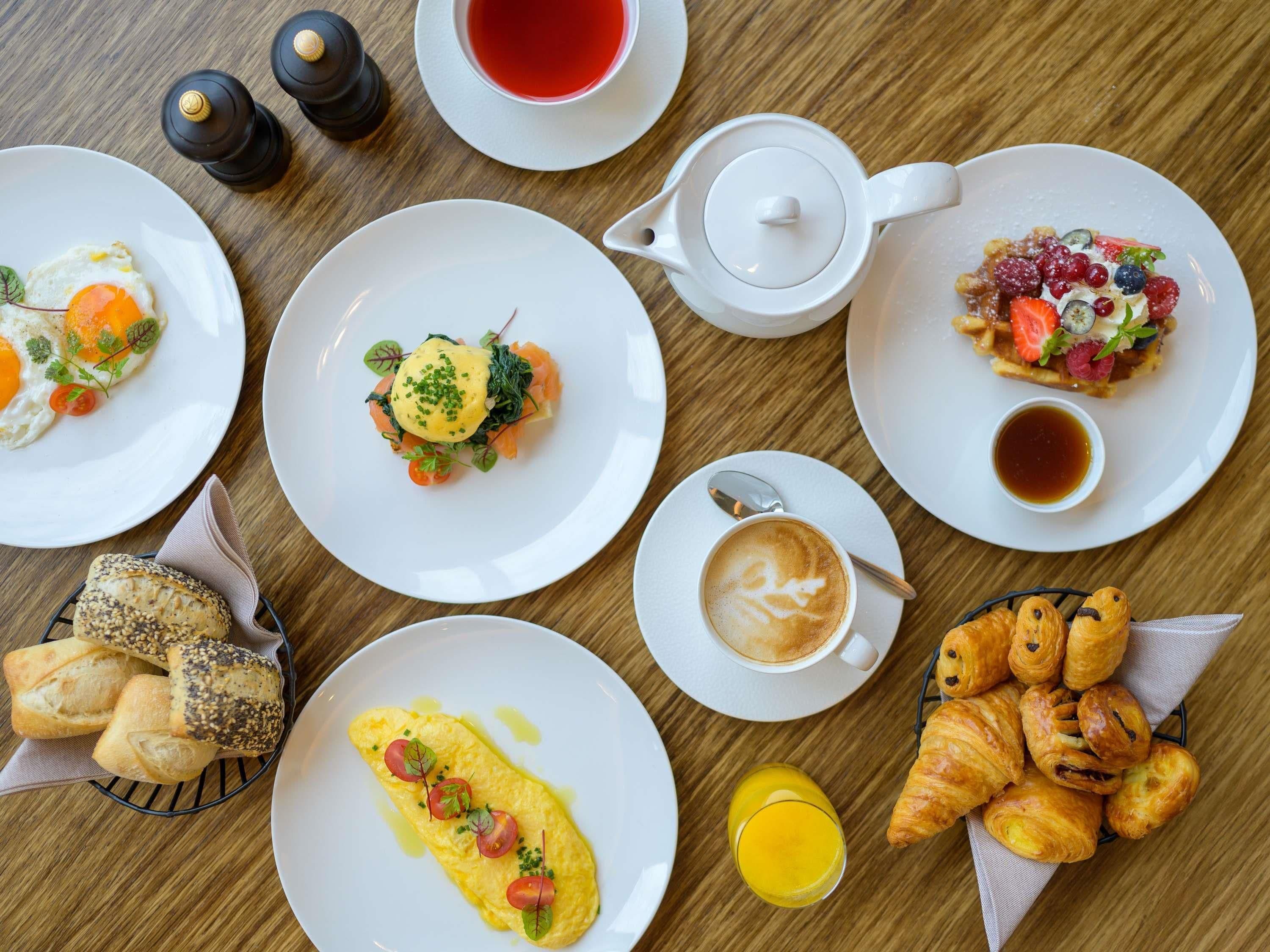 Una mesa de desayuno con diversos platos, entre ellos huevos, pasteles y una taza de té.