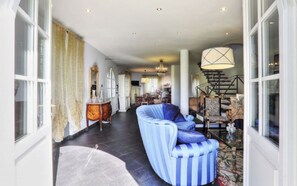 A spacious living area with a curved blue sofa, a chandelier, and a staircase with a decorative railing. - Beautiful villa with pool for relax and enjoy (Capannori, Lucca)
