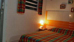 Ein Schlafzimmer mit einem Bett, einem Nachttisch, einer Lampe und einem Fenster mit Vorhängen.
