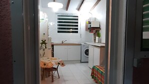 Eine Küche mit Essbereich, einer Waschmaschine und einem Bett mit bunter Decke.