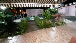 Ein überdachter Außenbereich mit gefliestem Boden, Topfpflanzen und einem Pool.