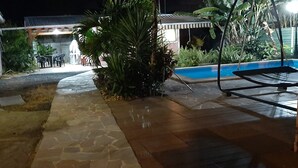 Ein gepflasterter Weg führt zu einem Poolbereich mit Sitzgelegenheiten und einer überdachten Terrasse.