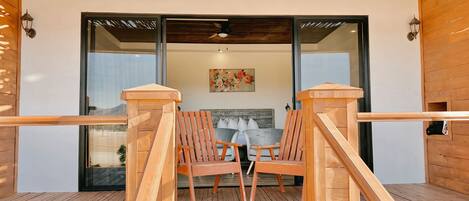 Una terraza de madera con un ventanal de vidrio que da a una habitación con una cama y un cuadro.