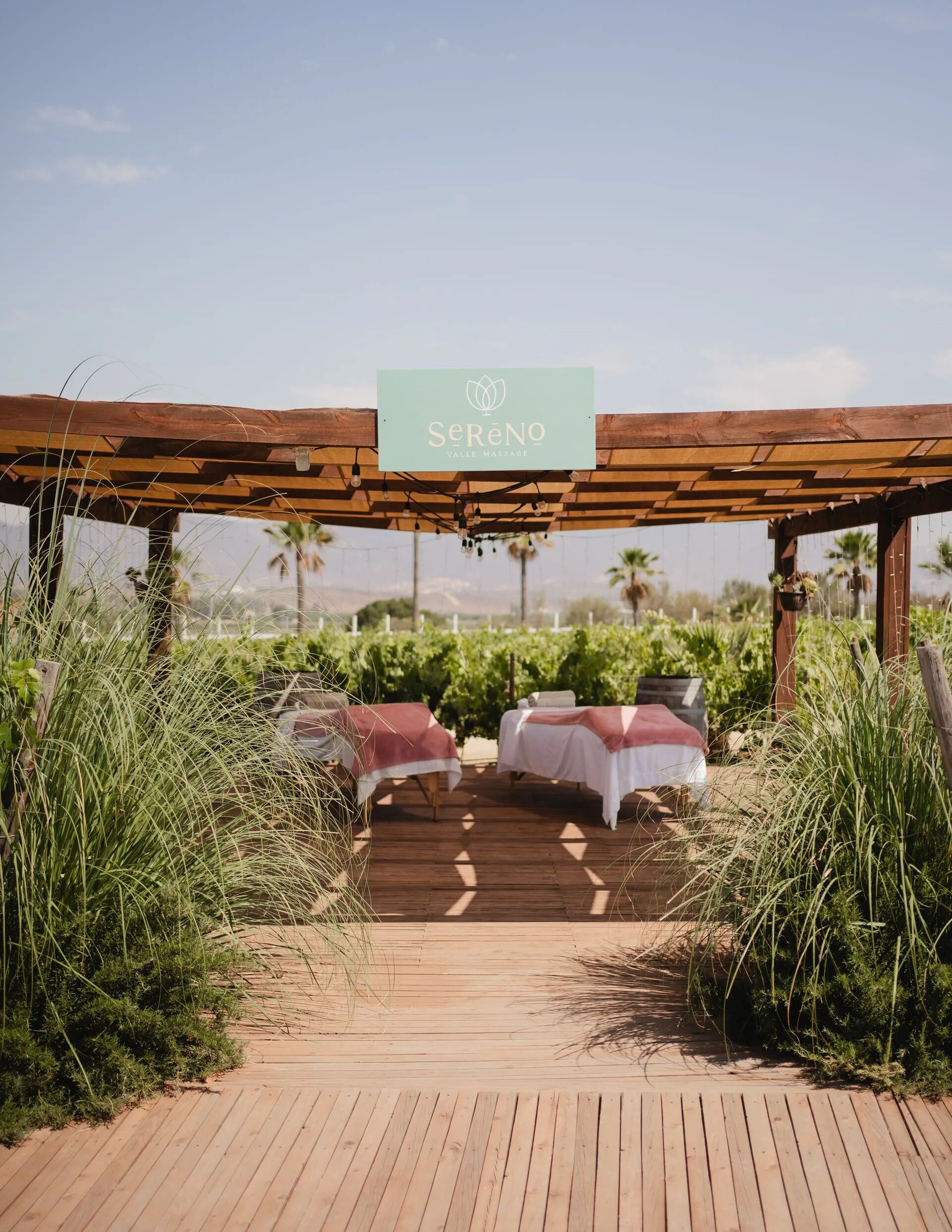 Una pérgola de madera con un letrero que dice "Sereno Valley Massage" y dos camillas de masaje debajo.