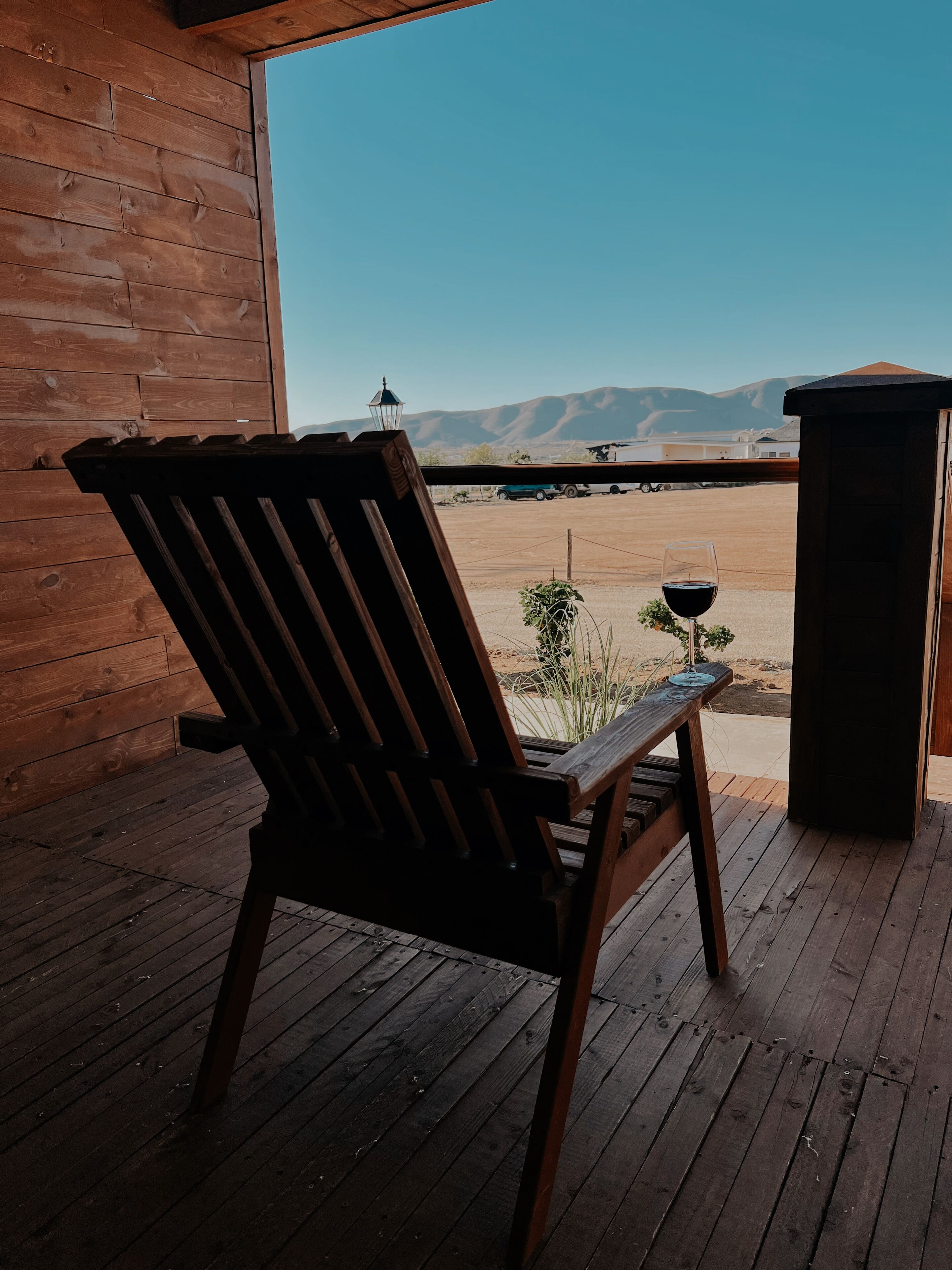 A wooden deck with a chair and a glass of red wine, overlooking a desert landscape with mountains.
