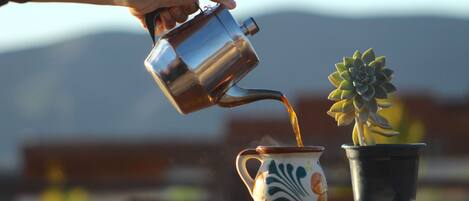 Una mano sirviendo café en una taza de cerámica, con una planta al lado.