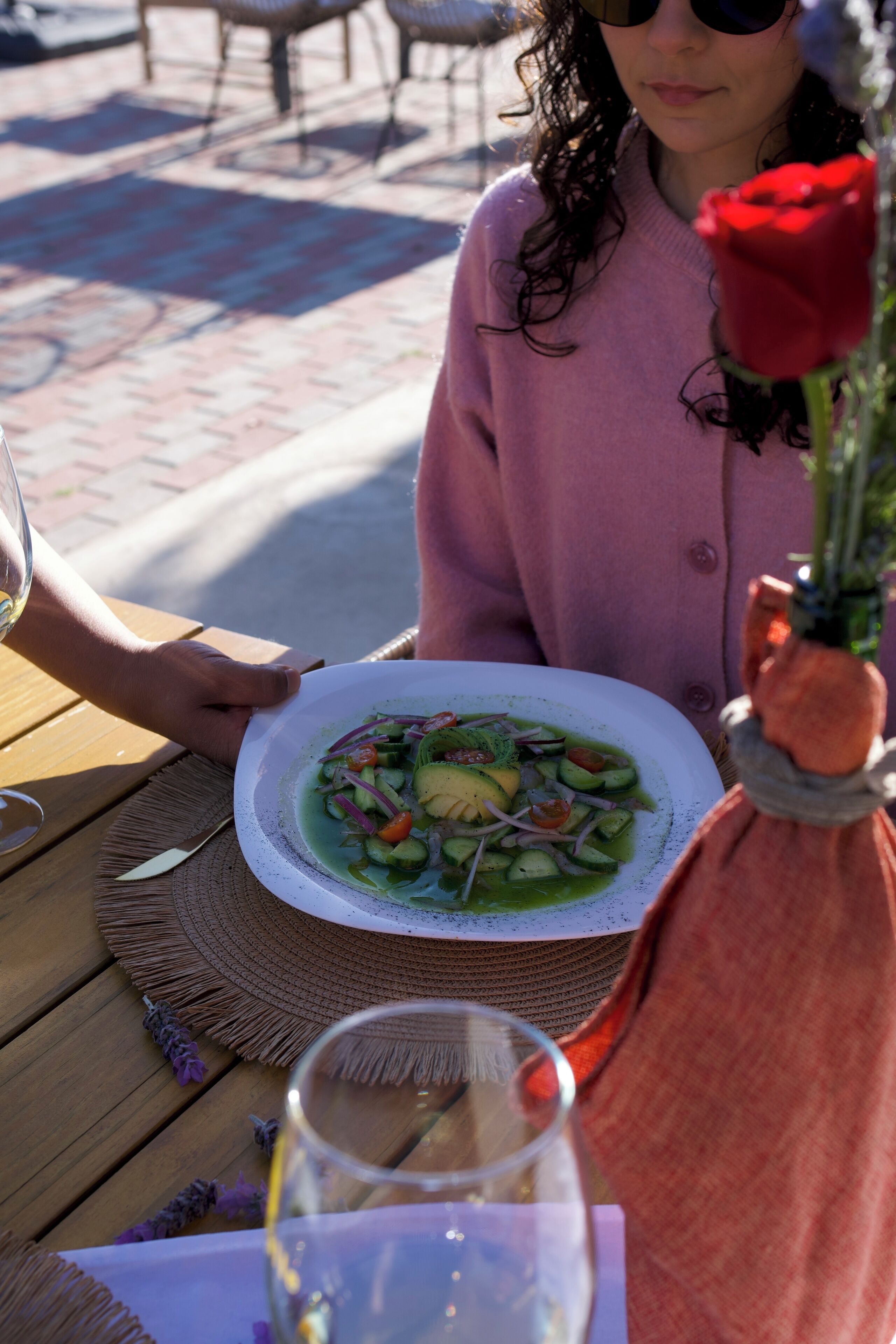 A dining table with a plate of food, a glass of water, and a rose.