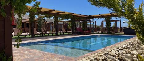Un área de piscina con sillones de descanso, una pérgola y un suelo de piedra.