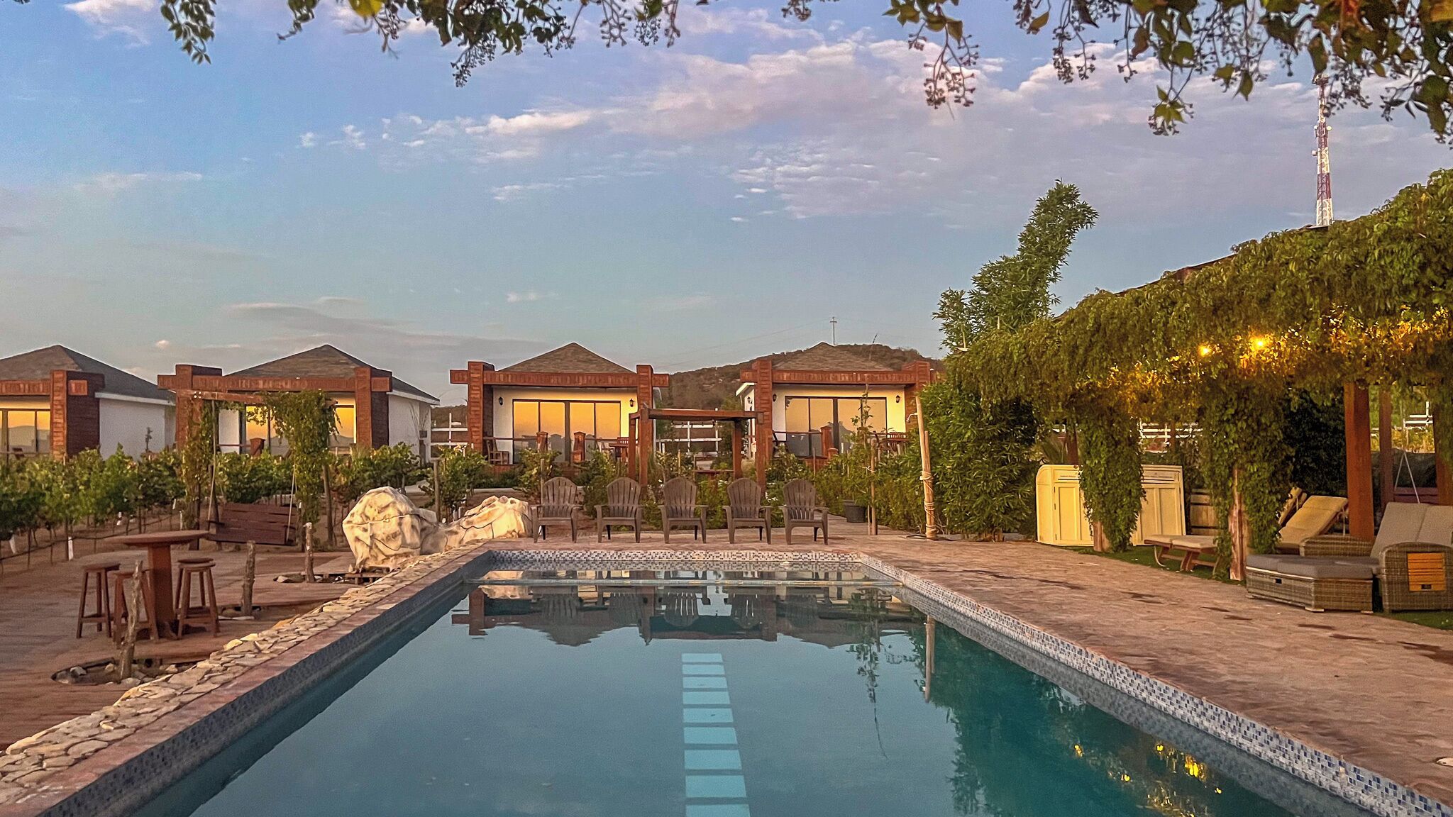 A pool area with lounge chairs, a pergola, and a view of the surrounding buildings.