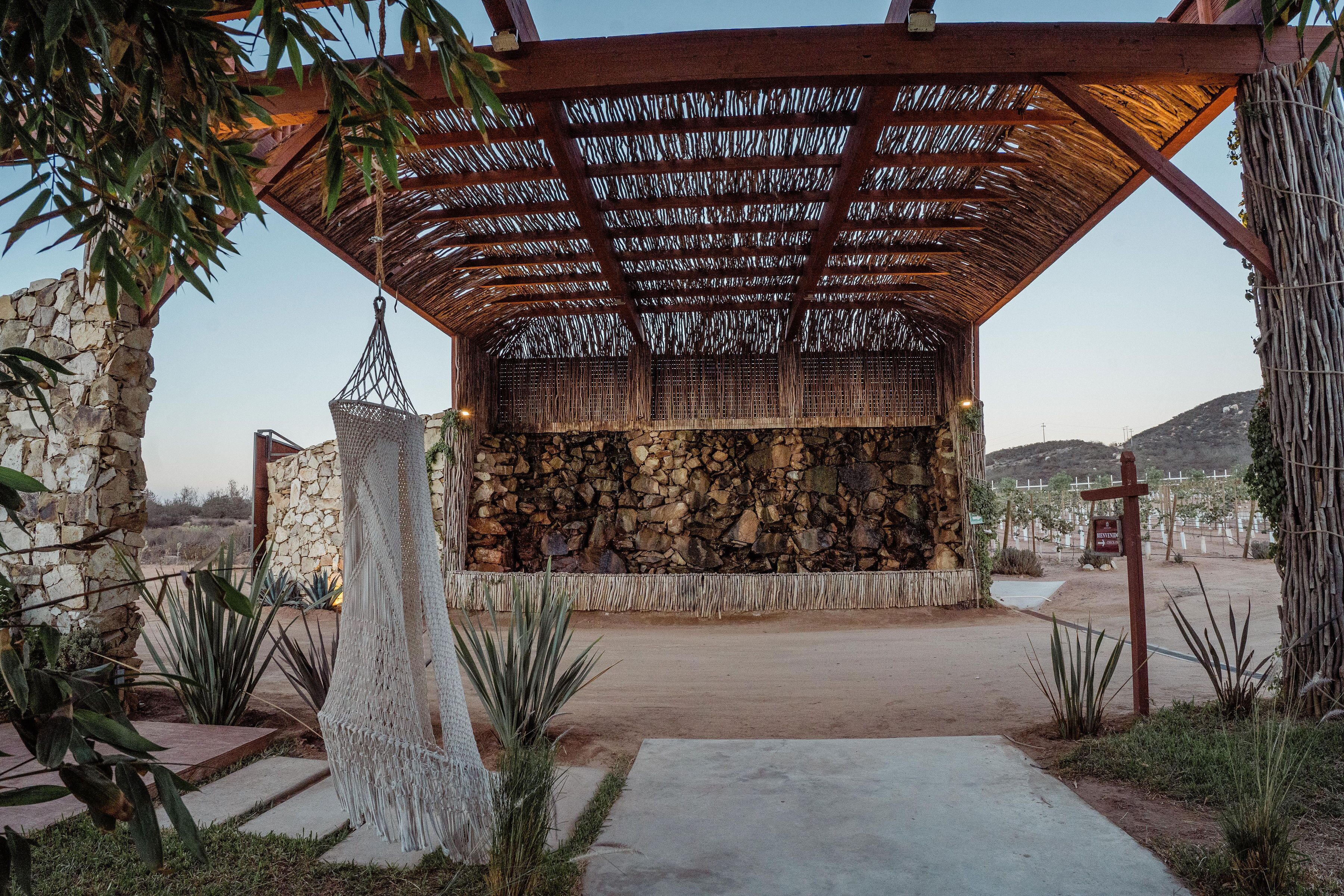 A covered outdoor area with a stone wall, a hanging macrame chair, and a pathway leading to a building.