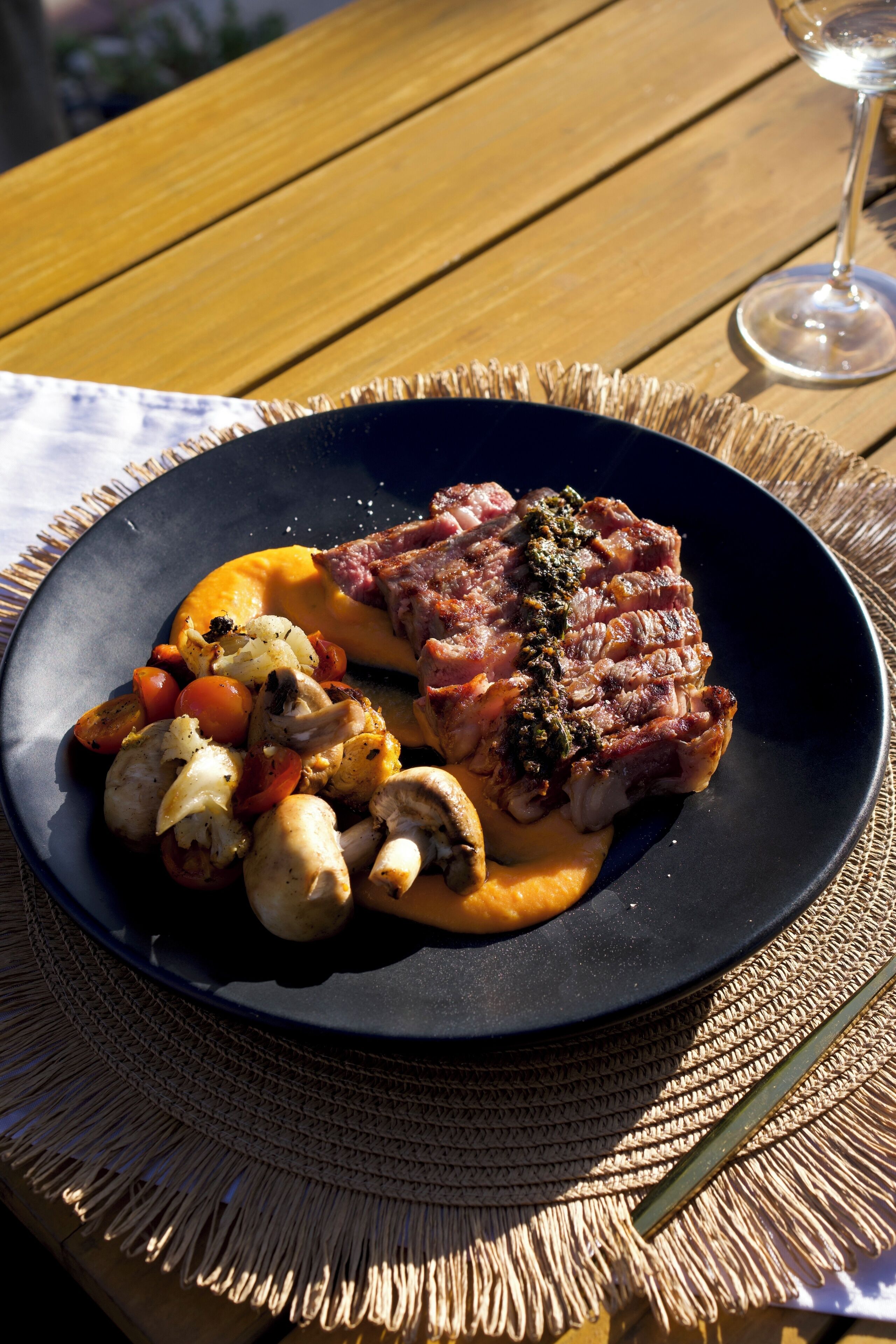 A plate of food with steak, mushrooms, and vegetables on a dark plate.