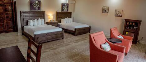 A hotel room with two beds, a wooden headboard, a red armchair, a small table, and a ceiling fan.