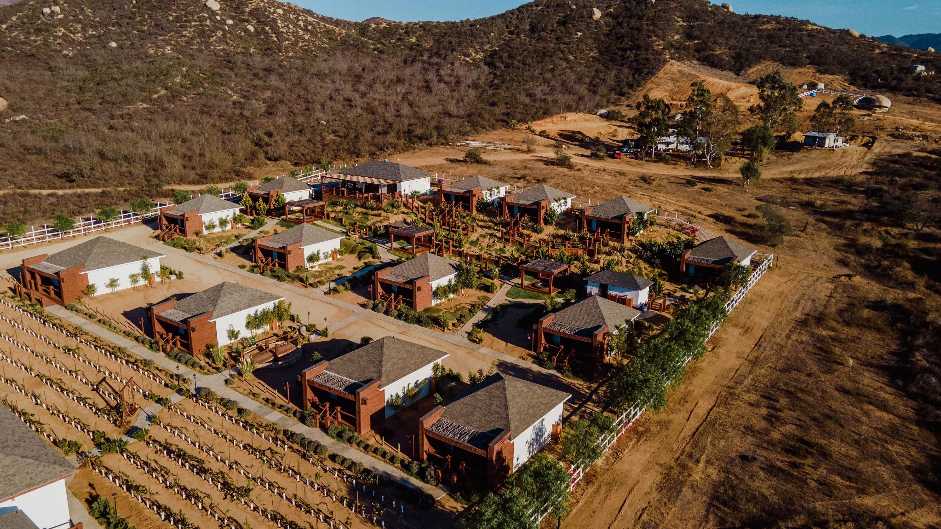 Un resort con varias construcciones tipo cabaña dispuestas en un patrón de cuadrícula, rodeado de jardines ajardinados y una zona de piscina.