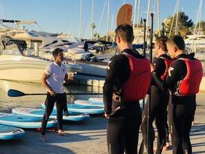 A group of people in wetsuits standing by paddleboards at a marina with boats in the background.