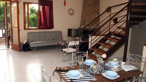 A dining area with a table set for four, a sofa, a TV, and a staircase. - Villa Olympia Skafidia beach (Skafidia Pirgos ilias)