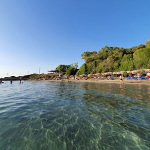 A beach with clear water, umbrellas, and people.