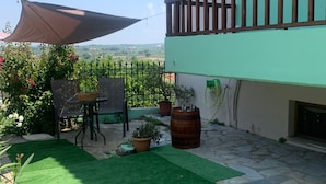A patio with artificial grass, a table with chairs, potted plants, and a wooden barrel. - Villa Olympia Skafidia beach (Skafidia Pirgos ilias)
