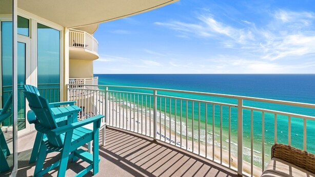 A balcony with a view of the ocean, turquoise chairs, and a wicker chair.