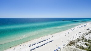A beach with a long pier extending into the ocean, rows of beach umbrellas, and a sandy shoreline.