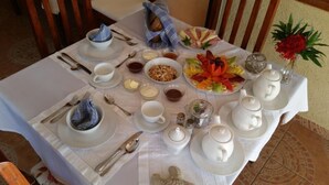 A breakfast table set with white tableware, including plates, bowls, cups, and cutlery. There is a fruit platter, a bowl of cereal, and various condiments. - Ecolodge Vistamar (Enriquillo)