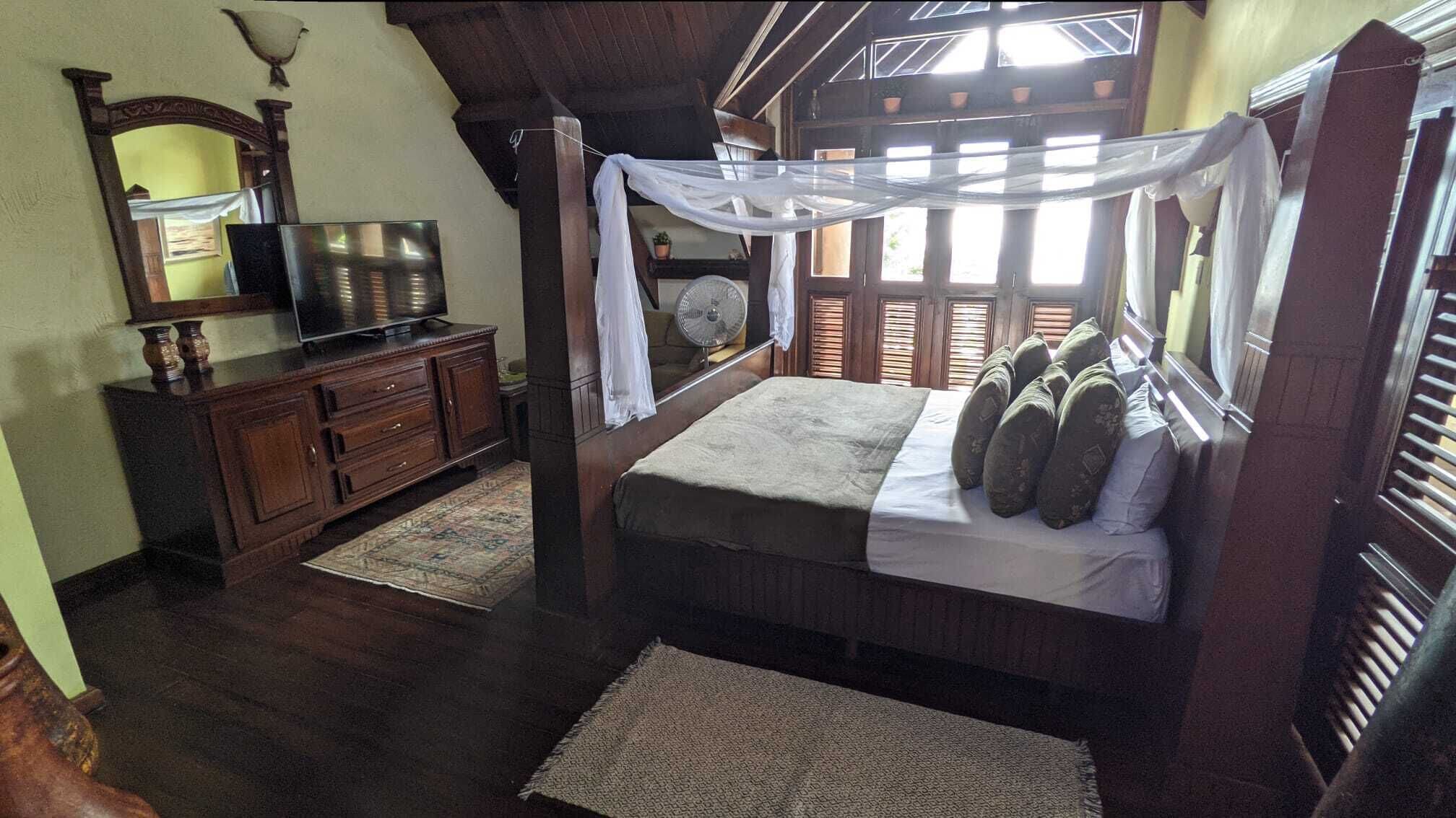 Un dormitorio con cama, televisor, cómoda y ventana con contraventanas.