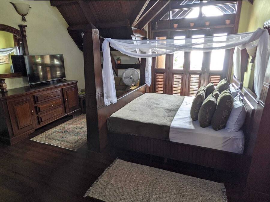 Un dormitorio con cama, televisor, cómoda y ventana con contraventanas.