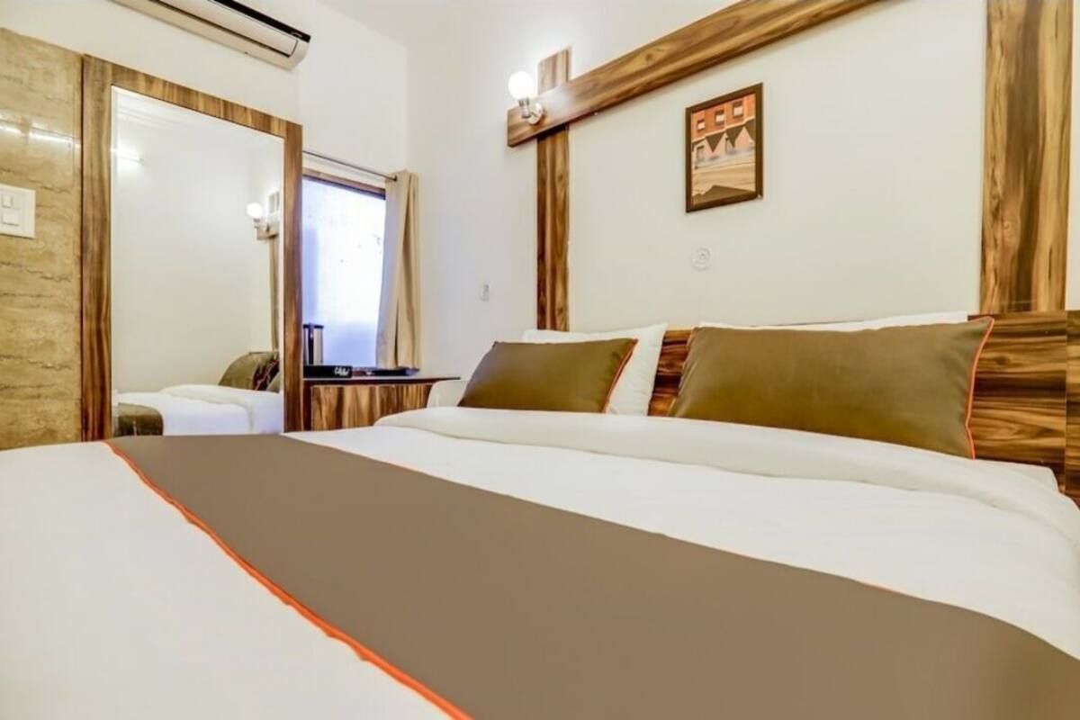 Habitación de hotel con una cama grande, cabecera de madera, una mesita y una lámpara de pared.