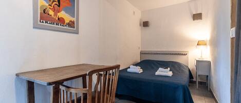 A hotel room with a bed, a desk, a chair, a nightstand, and a lamp.